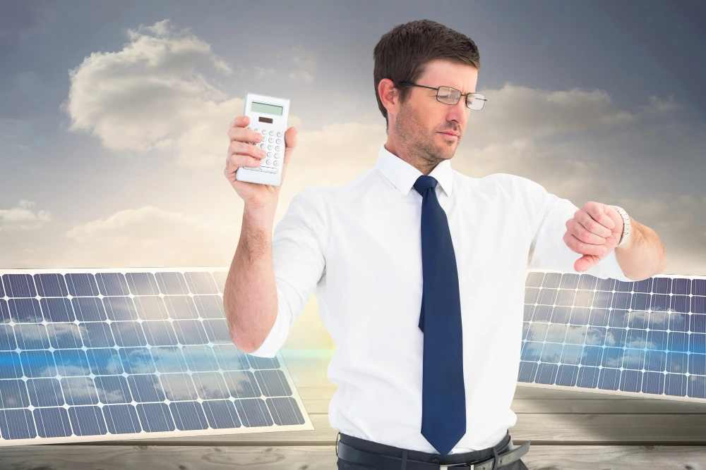 Man in business attire holding calculator while comparing solar panel installation costs and savings with solar panels in background